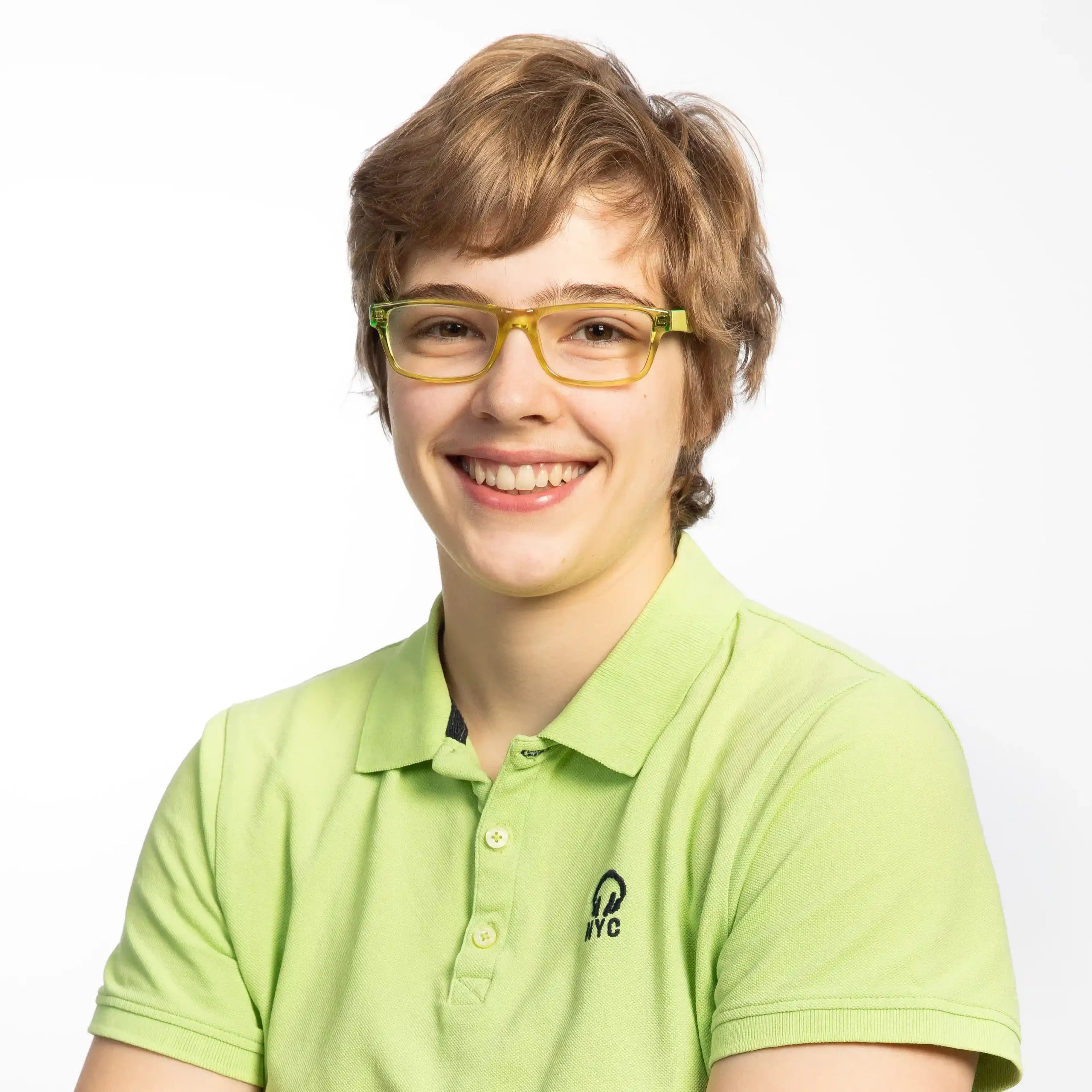 Eine lächelnde Person mit kurzen hellbraunen Haaren und einer grünen Brille, die ein hellgrünes Hemd mit Kragen und einem kleinen schwarzen NYC-Logo trägt, vor einem schlichten weißen Hintergrund.