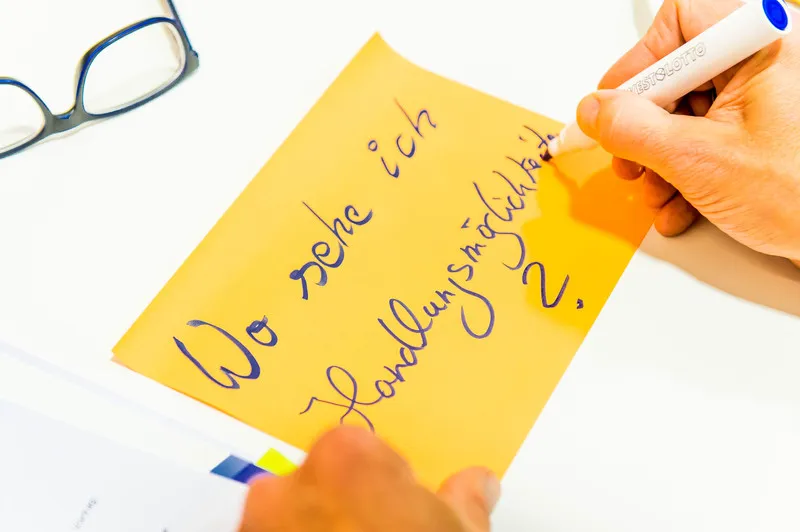 BSJ_Praevention sexualisierter- interpersonaler-Gewalt Jemand schreibt mit blauer Tinte auf gelbem Papier: „Wo sehe ich Handlungsmöglichkeiten?“; daneben liegen eine Brille und Unterlagen.
